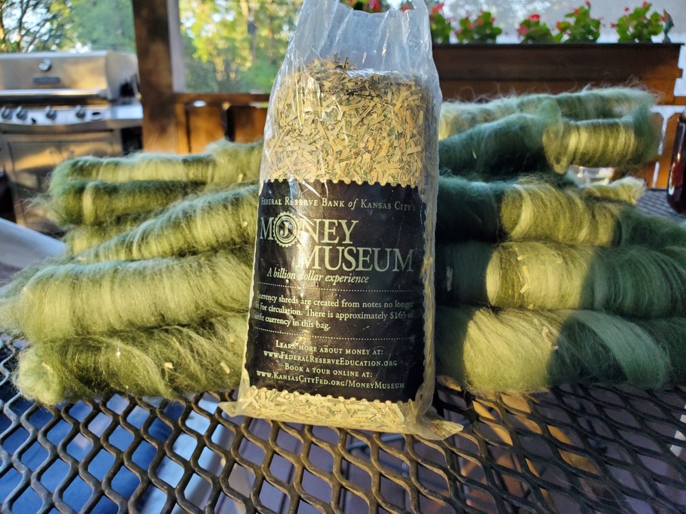 A bag of shredded money with a stack of green rolags behind it