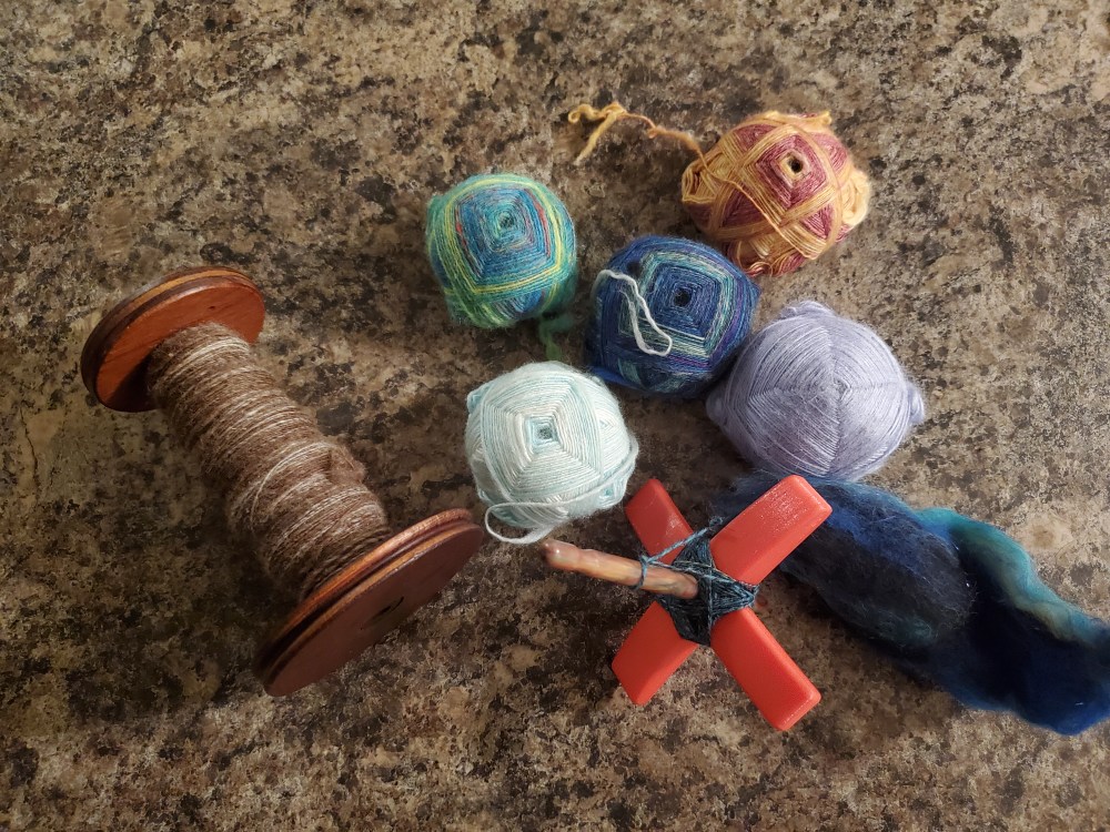 A bobbin half full of a tweedy brown yarn, five Turkish turtles in assorted colors, and a Turkish drop spindle.