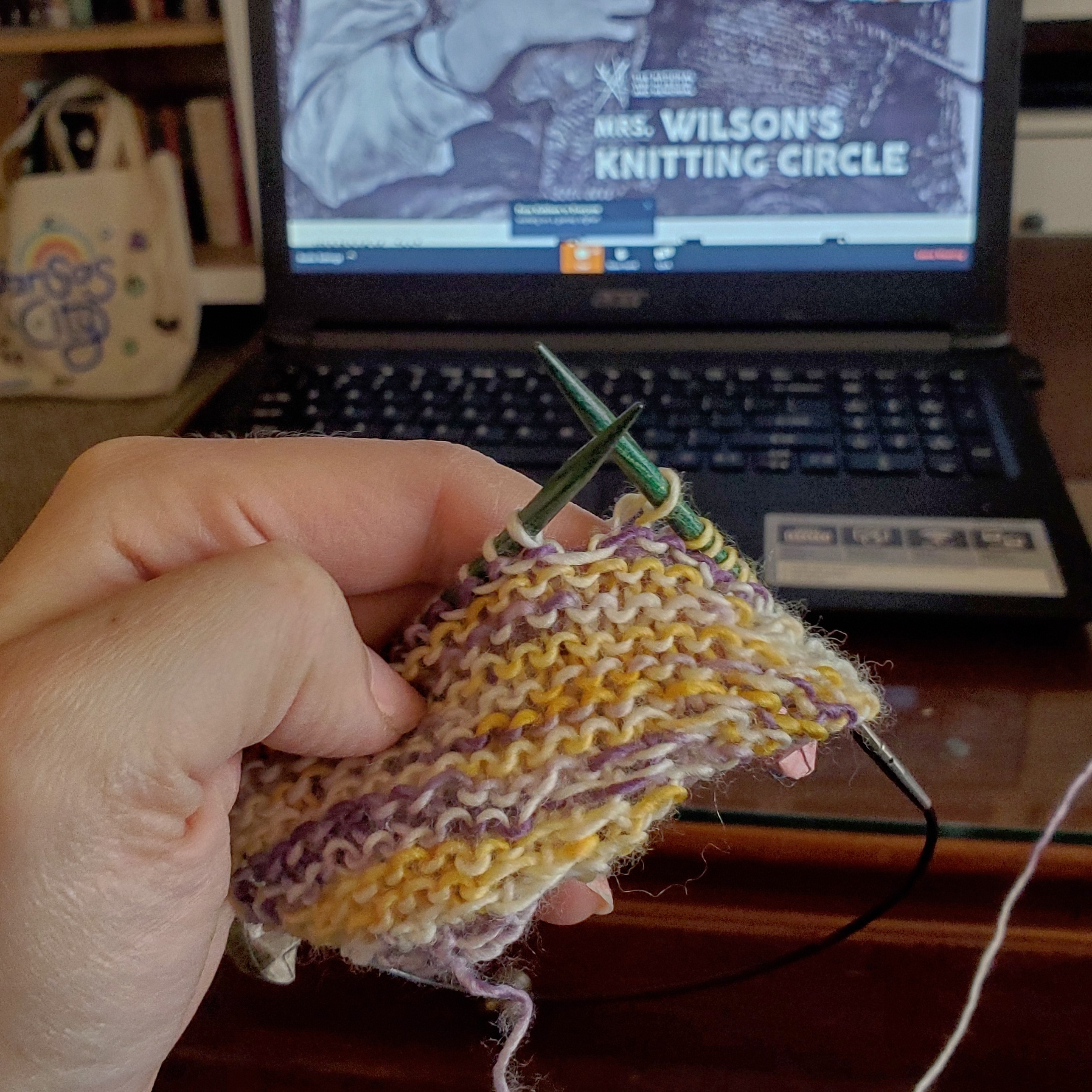 A small, triangle knitting project in front of a computer
