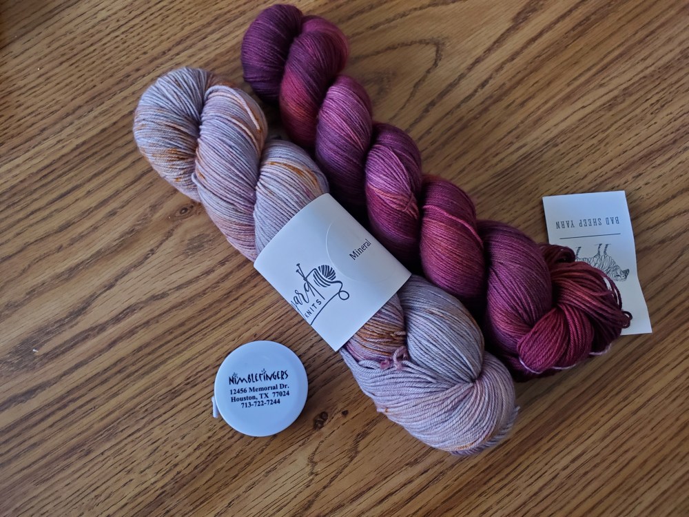 Two hand-dyed skeins of yarn with a nimblefingers tape measure