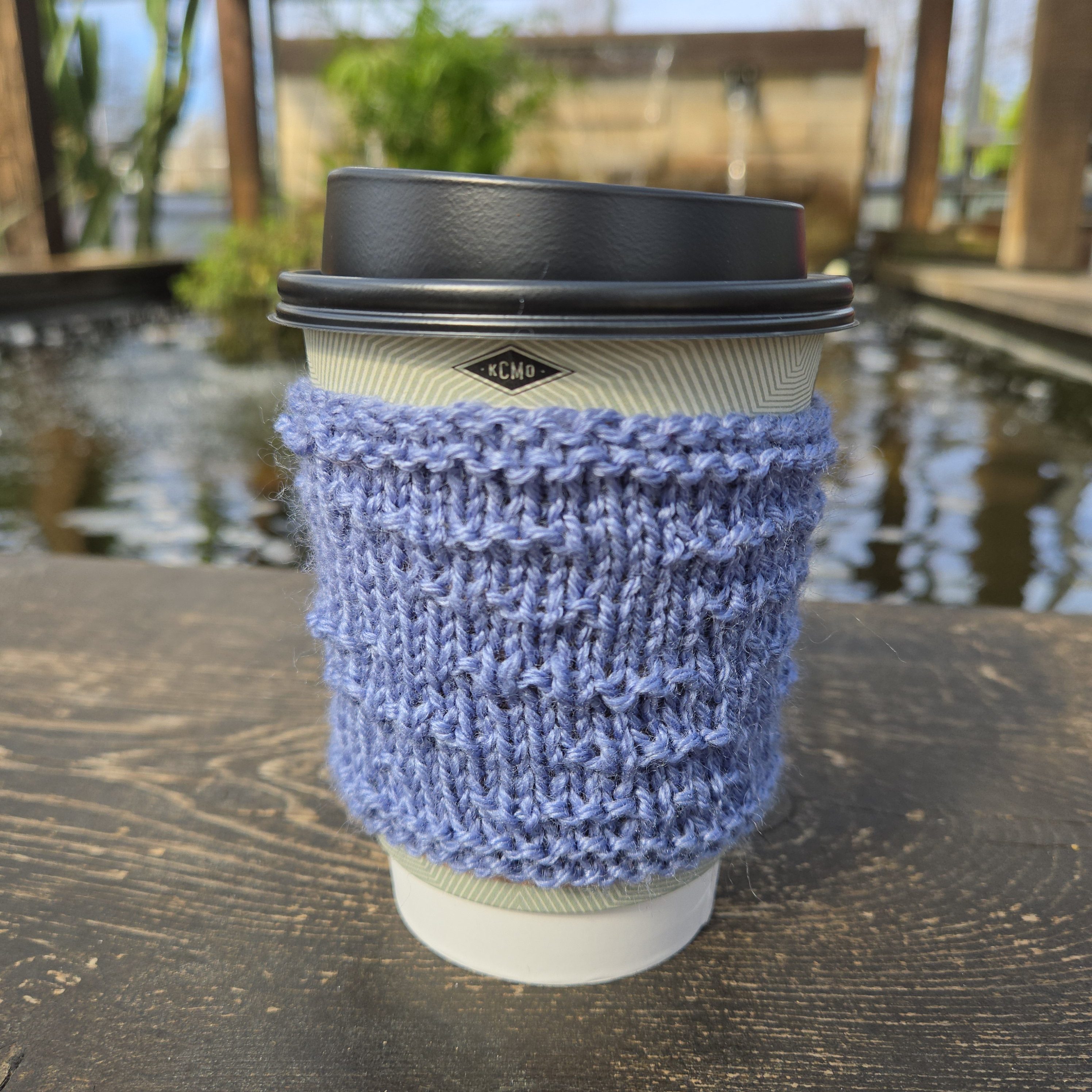 Four-Letter Word Coffee Sleeve in front of pond
